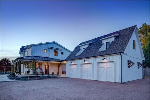Weisleder Residence: a white board-and-batten farmhouse and garage at dusk